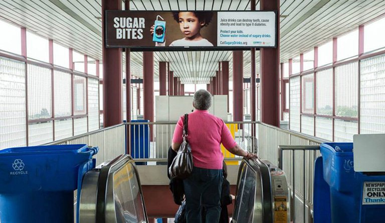 Women Going Down An Escalator Under An Anti-Sugar Campaign Poster