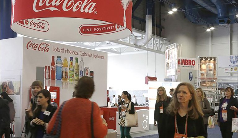 Patrons Walking By A Coca-Cola Kiosk At A Conference
